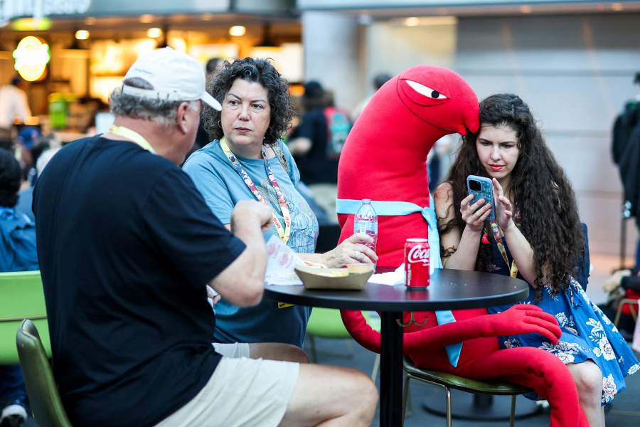 A person sits on their phone with a life-size plush of Allan, a character from the series Smiling Friends, during the opening day of New York Comic Con at the Jacob Javits Center in Manhattan in New York City, US, October 8, 2026